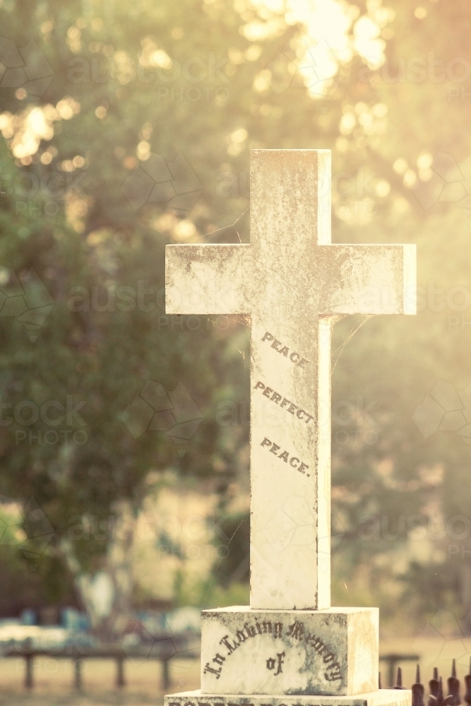 Sunlight hitting a cross on top of a gravestone - Australian Stock Image