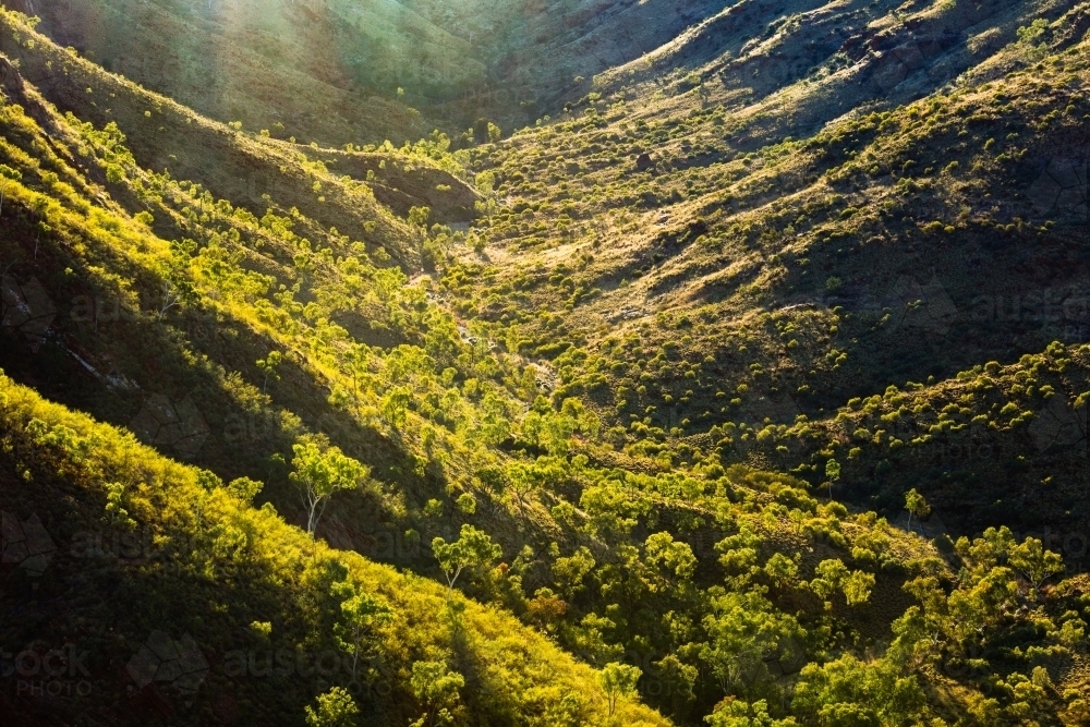 Sunlight illuminating a small valley in the West MacDonnell Ranges. - Australian Stock Image