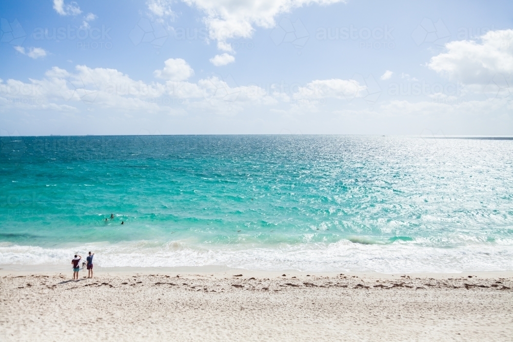Sunlight on beach with distant people swimming in water and watching the waves - Australian Stock Image