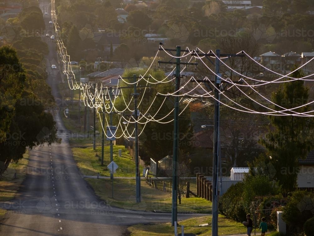 Sunlight on power lines looping off into the distance in a town - Australian Stock Image
