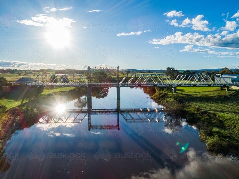 Sunlight over Paterson River with historical timber truss bridge scene reflected in water - Australian Stock Image