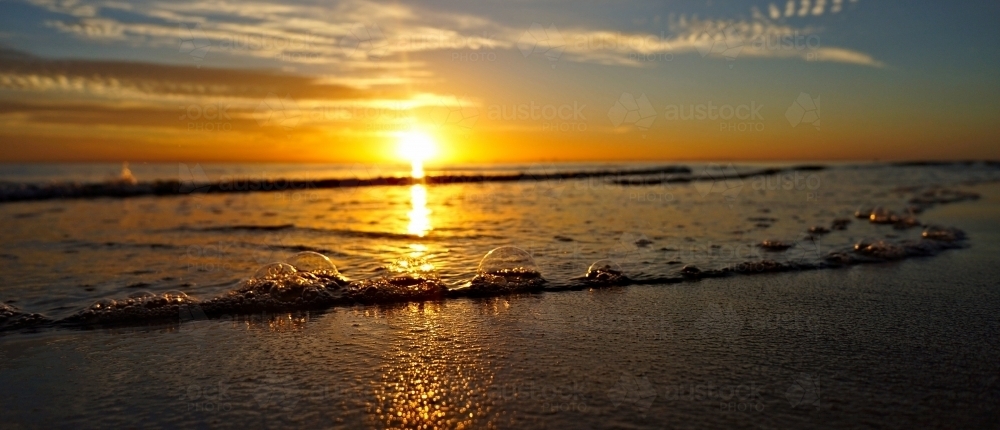 Sunlight reflecting on bubbles on the sand as the tide goes out - Australian Stock Image
