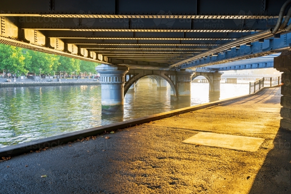 Sunlight shining on a pathway under a wide steel bridge - Australian Stock Image