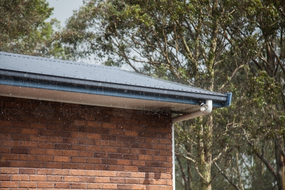 Sunlight shining on rain falling on tin roof of house - Australian Stock Image