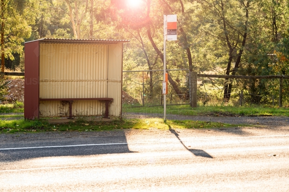 Sunlight shining through trees behind a bus shelter on a roadside - Australian Stock Image