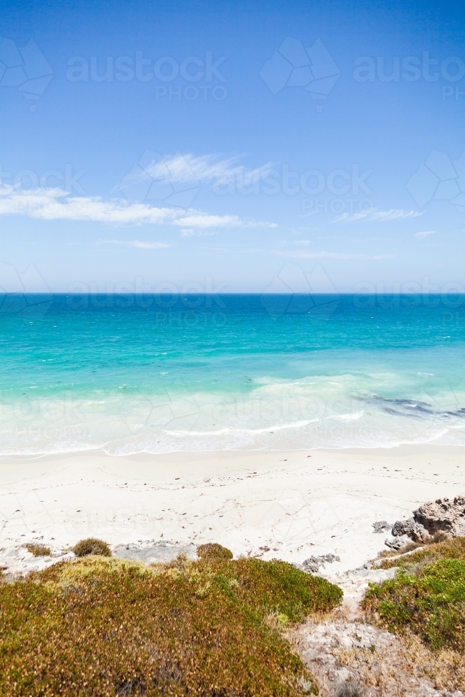 Sunlit coastland with view of shrubs, beach and clear blue coastal waters - Australian Stock Image