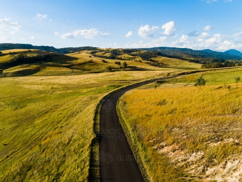 Sunlit country road in rural paddock landscape - Australian Stock Image