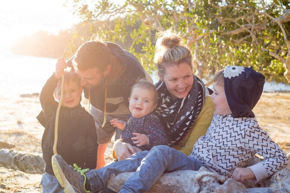 Sunlit family of five sitting together outdoors by a lake - Australian Stock Image