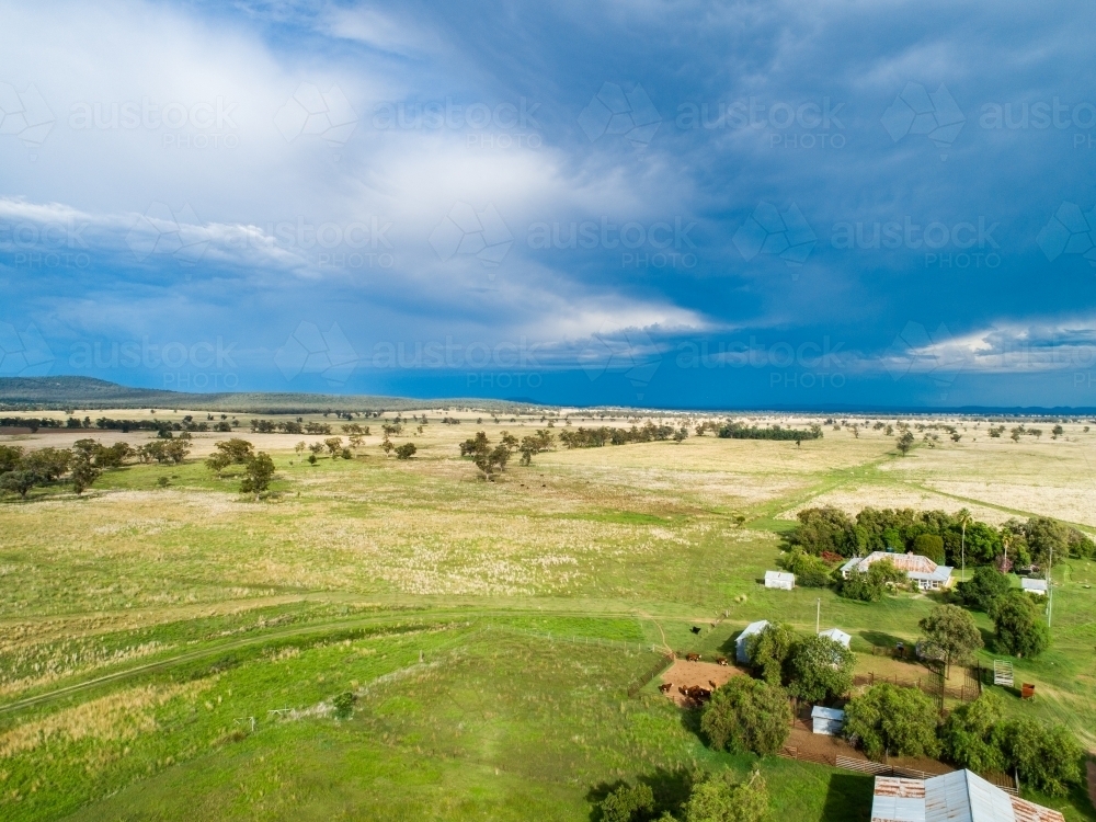 Sunlit farmland with cattle yards and dark sky full of rain cloud above - Australian Stock Image