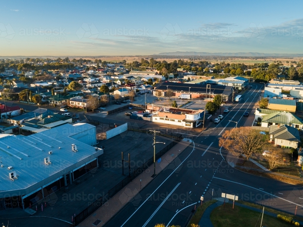 sunlit shops and buildings in small town at sunrise with road intersection - Australian Stock Image