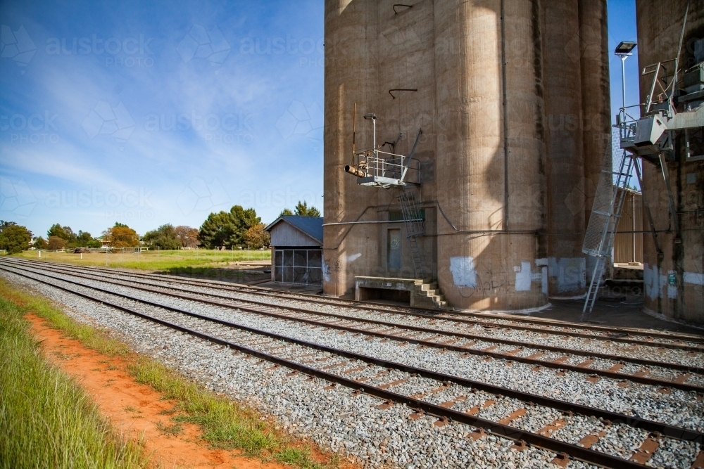 Sunlit train tracks running beside wheat silo infrastructure - Australian Stock Image