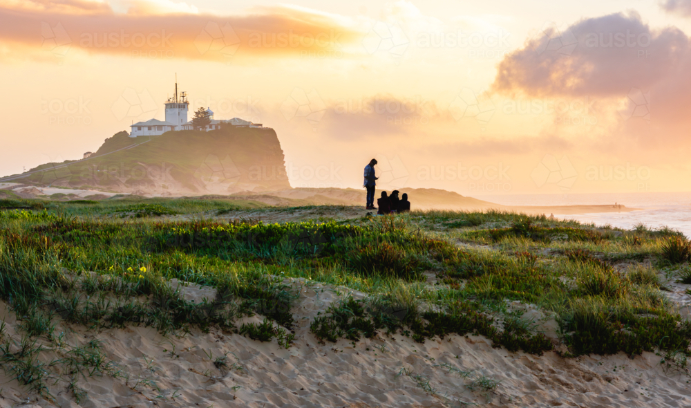 Sunrise at Nobby's Beach with Nobby's Lighthouse in the Background and a Family in the Midground - Australian Stock Image