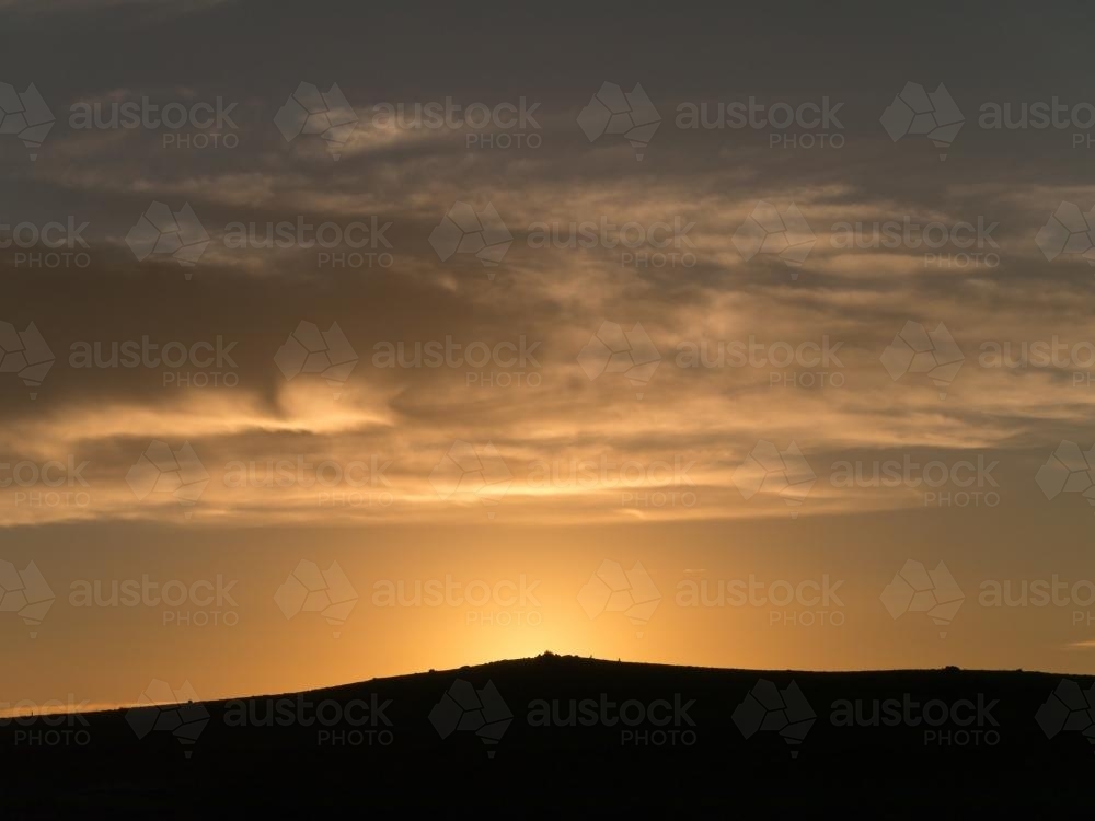 Sunrise over a small hill with light cloud - Australian Stock Image