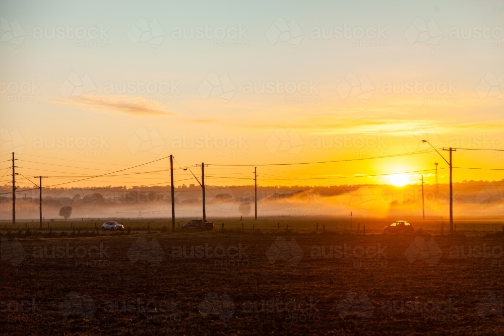 Sunrise over misty paddocks and busy road with morning rush traffic and power poles - Australian Stock Image