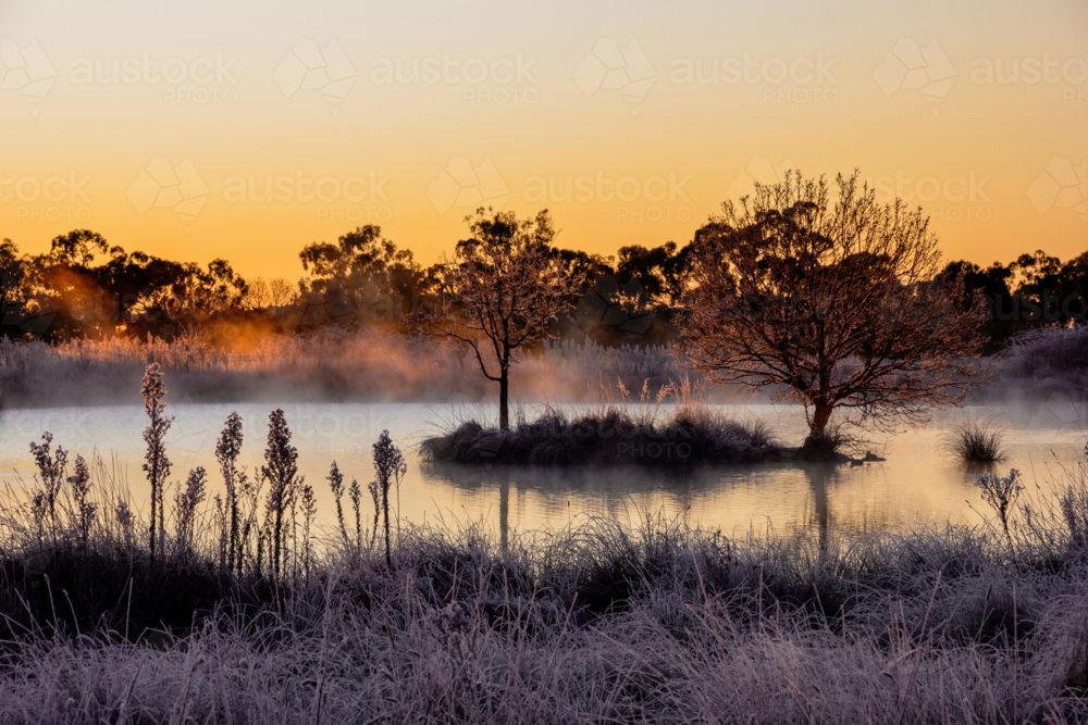 Sunrise serenity, fog illuminated by dawn light over dam on a frosty winter’s morning - Australian Stock Image