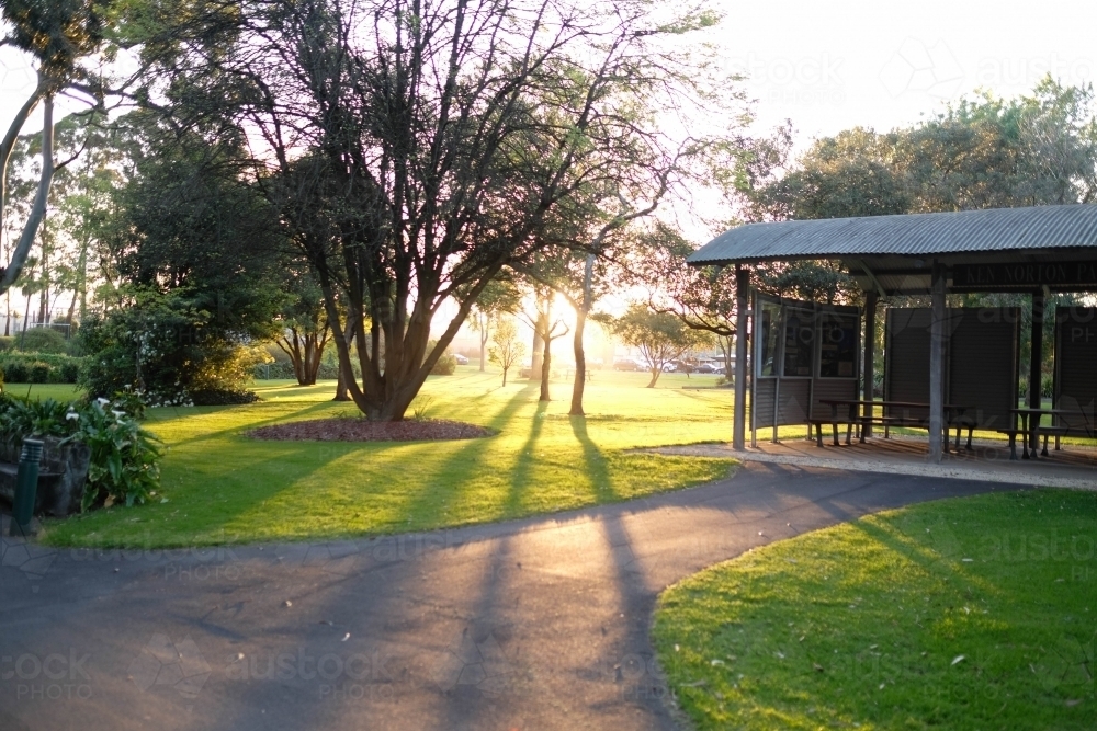 Suns setting behind park with trees and shelter - Australian Stock Image