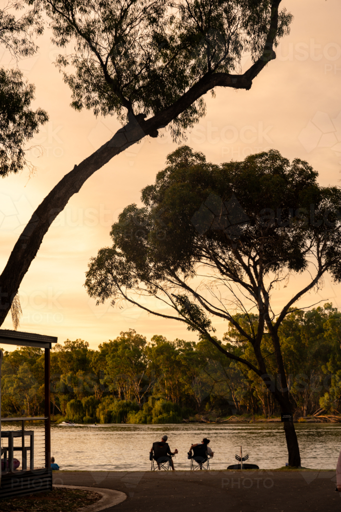 sunset at river with trees and water, people and ski boats silhouetted - Australian Stock Image