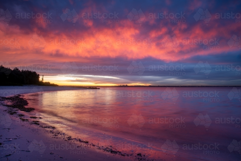 Sunset colours over a curve of beach - Australian Stock Image