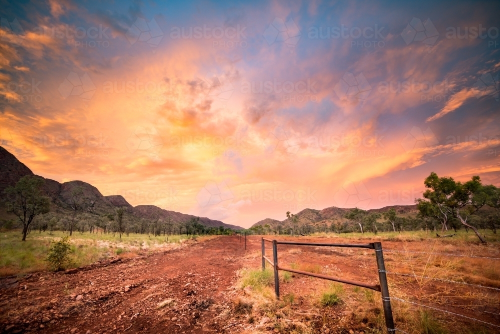 Amazing pastel sunset in the Kimberley with fence leading along a dirt road - Australian Stock Image