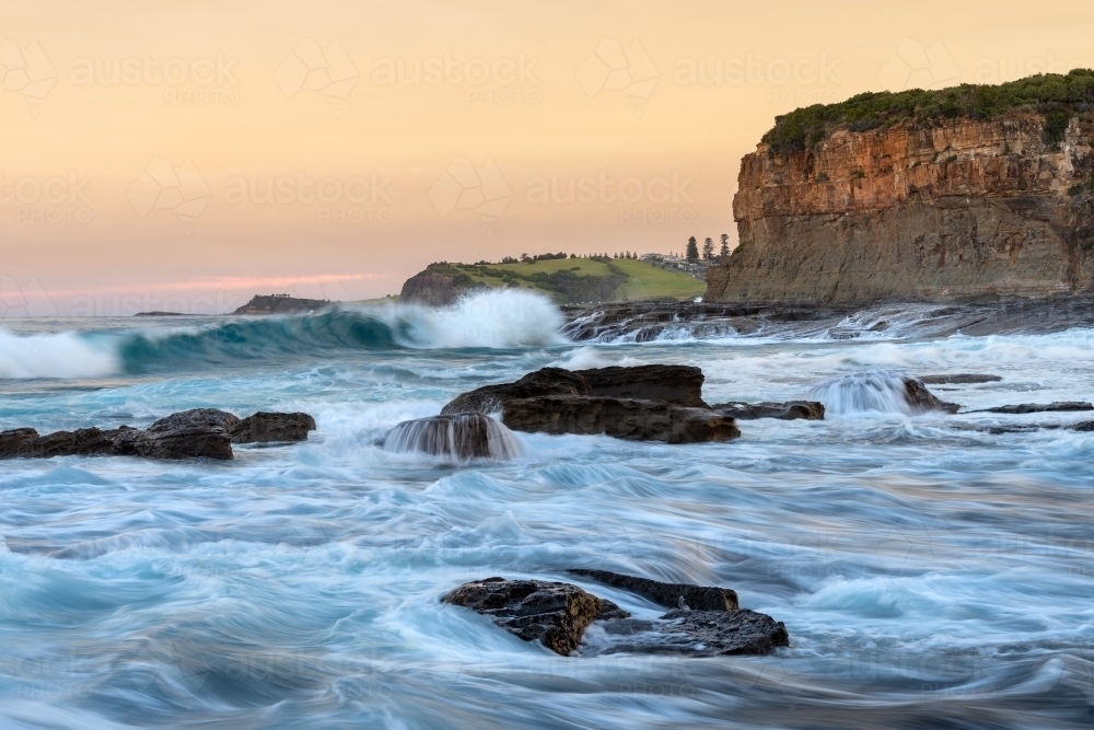 Sunset landscape of the ocean surging around a rocky headland - Australian Stock Image