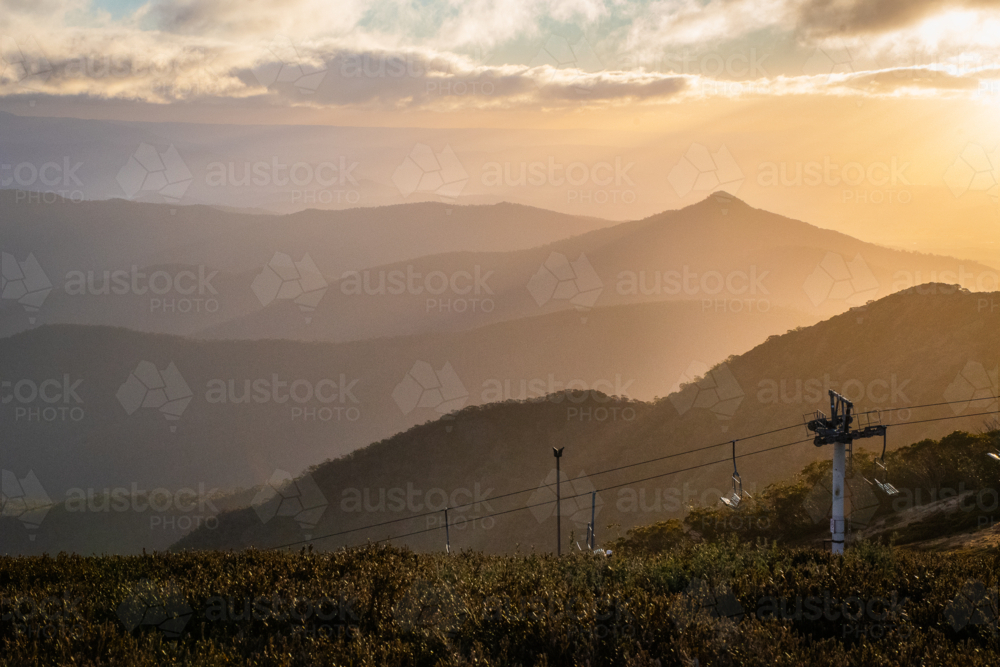 Sunset on Mt Buller with ski lift in shot and green foliage in foreground - Australian Stock Image
