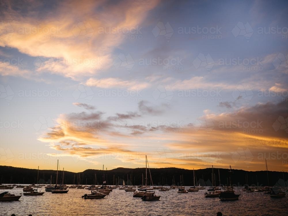 Sunset over boats on harbour with mountains behind - Australian Stock Image