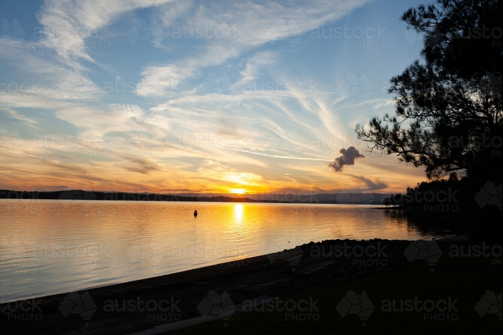 sunset over water of lake Macquarie with buoy on calm water on peaceful evening - Australian Stock Image