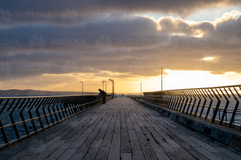 Sunset views along a wooden pier with a person silhouetted against the horizon. - Australian Stock Image