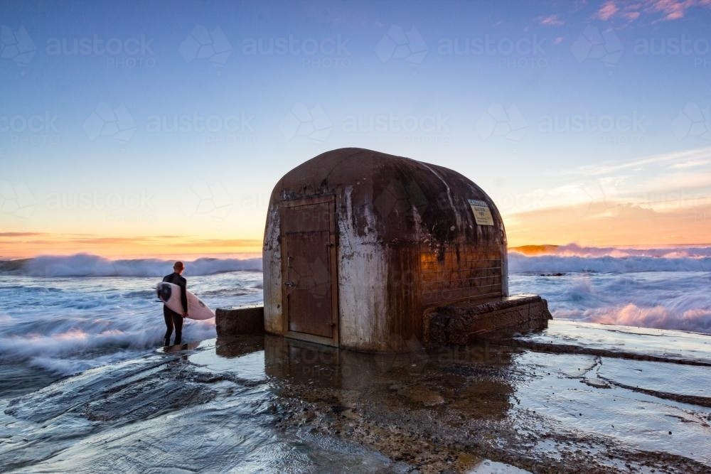 Surfer and ocean baths pump house at sunrise - Australian Stock Image