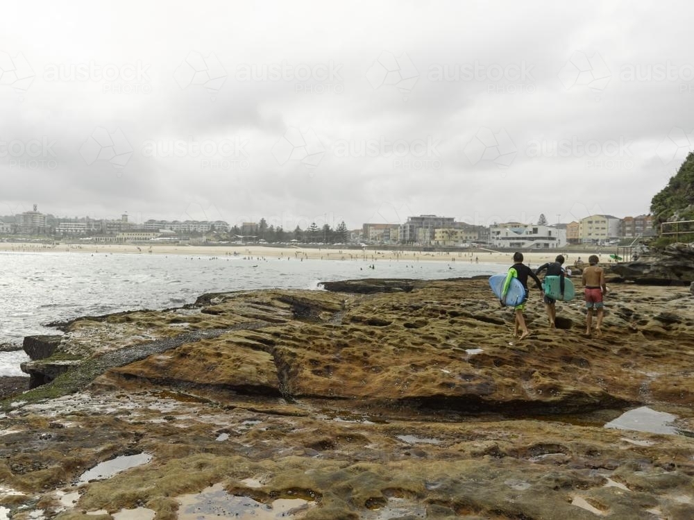 Surfer boys walking on rocks at Bondi Beach on an overcast day - Australian Stock Image