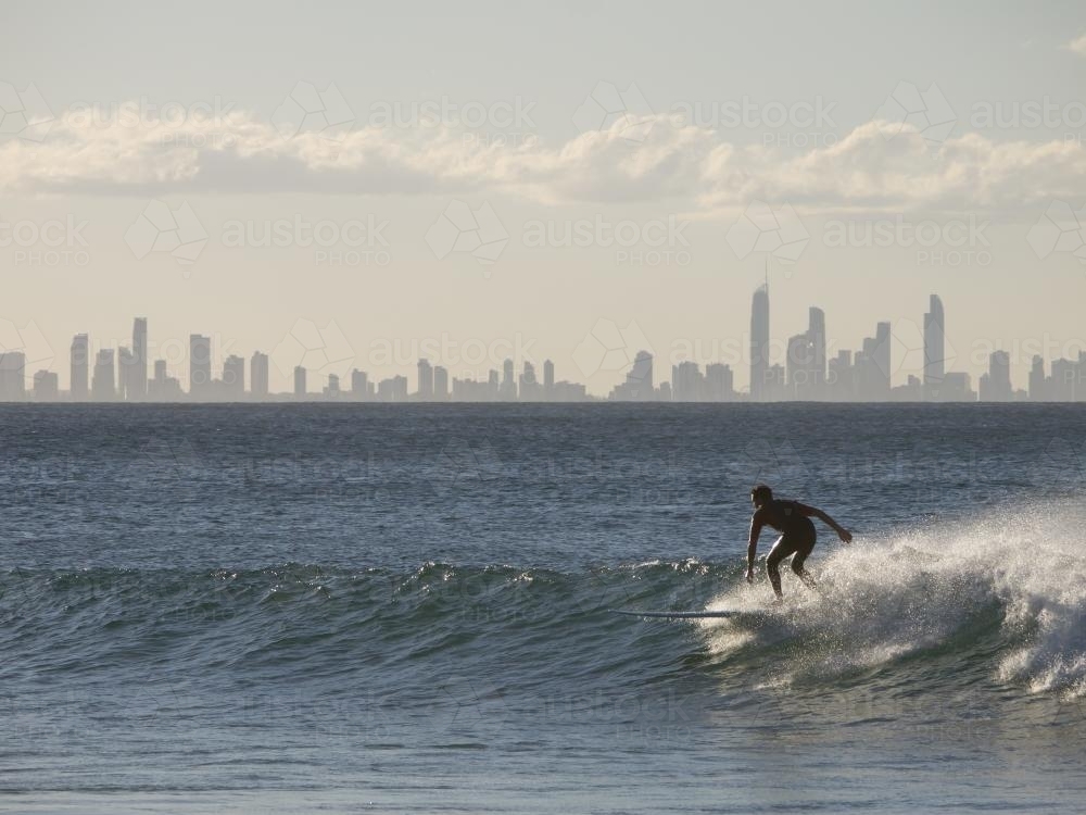Surfer catching a wave with skyline of high-rise buildings in the background - Australian Stock Image