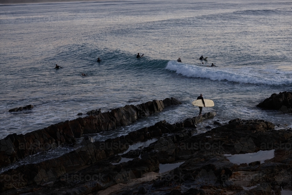 Surfer heading out off rocks in ocean on sunrise - Australian Stock Image
