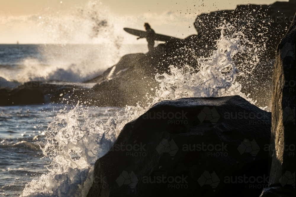 surfer on the rocks with crashing waves - Australian Stock Image