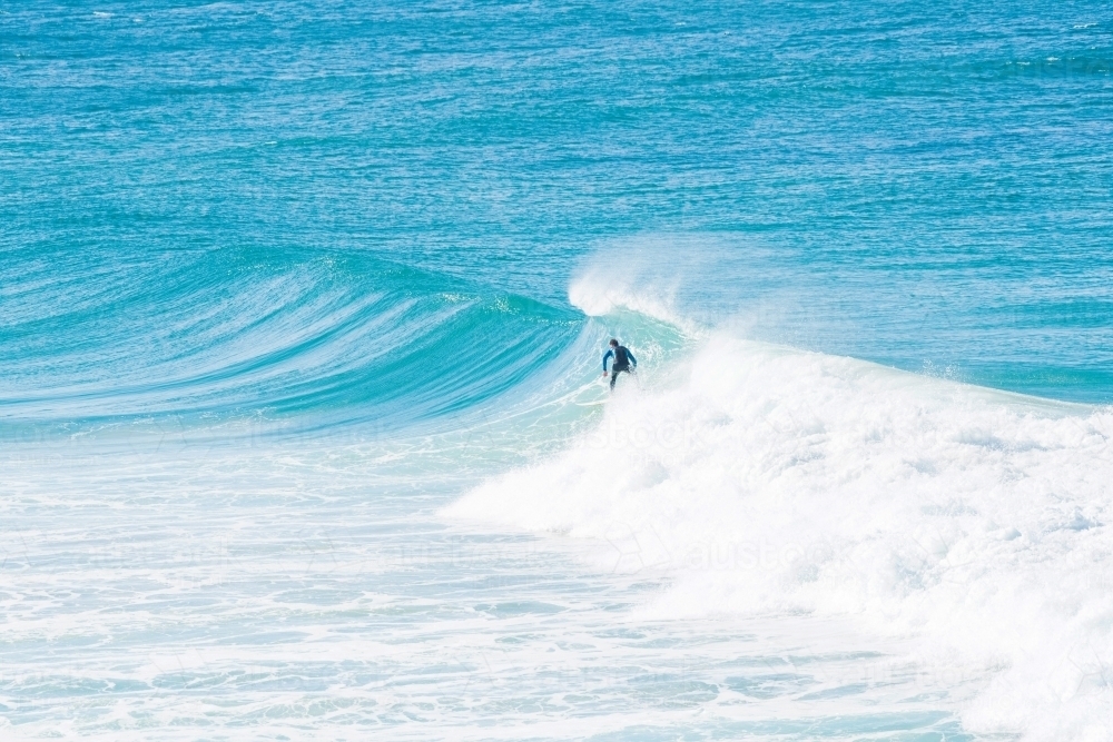 Surfer riding a wave in the clear blue ocean - Australian Stock Image