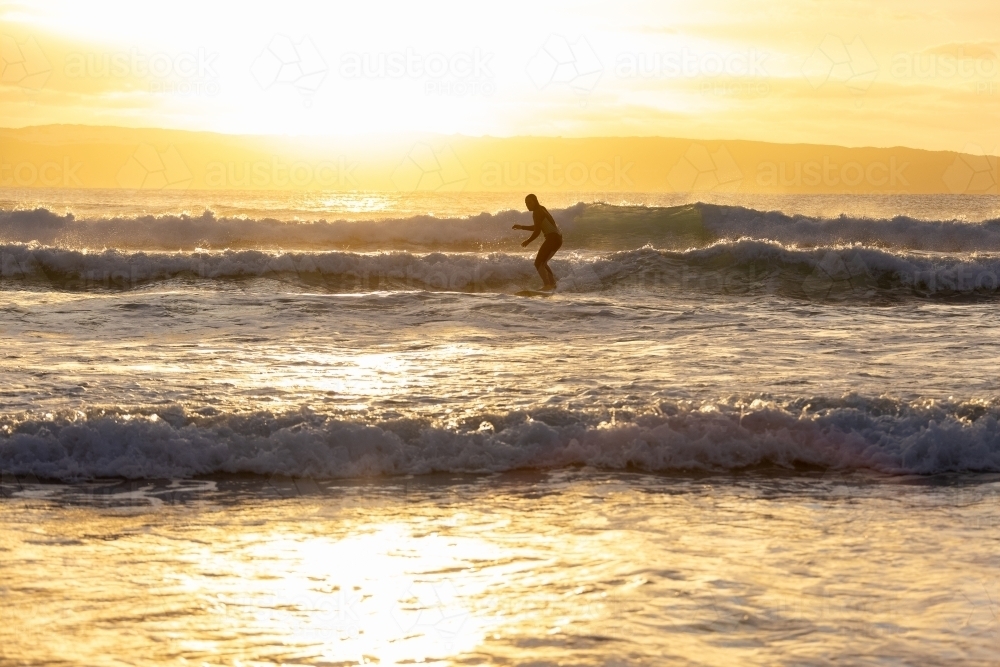 surfer standing on board catching a wave at sunset - Australian Stock Image