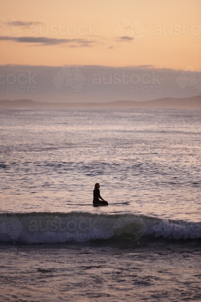 Surfer waiting for waves in ocean on sunrise - Australian Stock Image