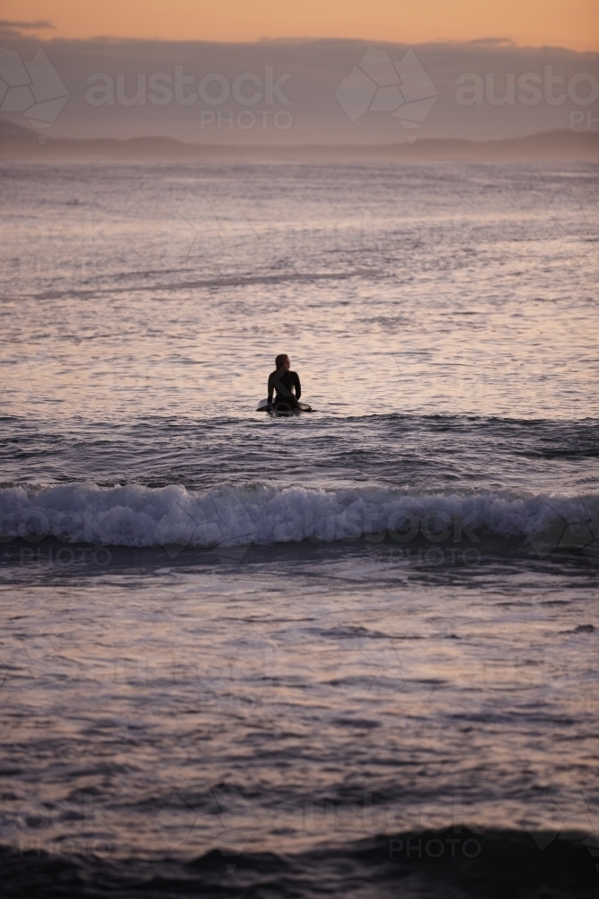 Surfer waiting for waves in ocean on sunrise - Australian Stock Image