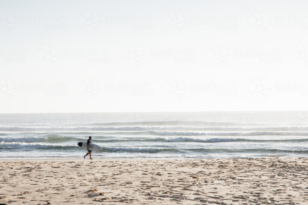 Surfer walking along beach in the early morning - Australian Stock Image