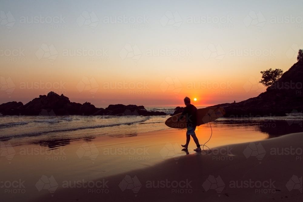 Surfer walking the beach at sunrise - Australian Stock Image