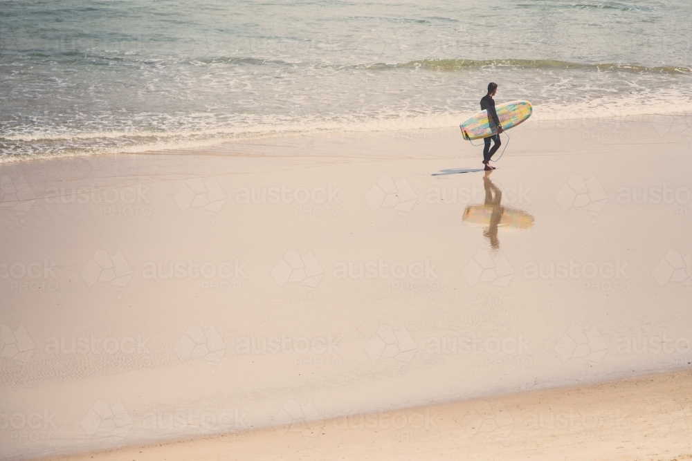 Surfer walking the water line at a beach - Australian Stock Image