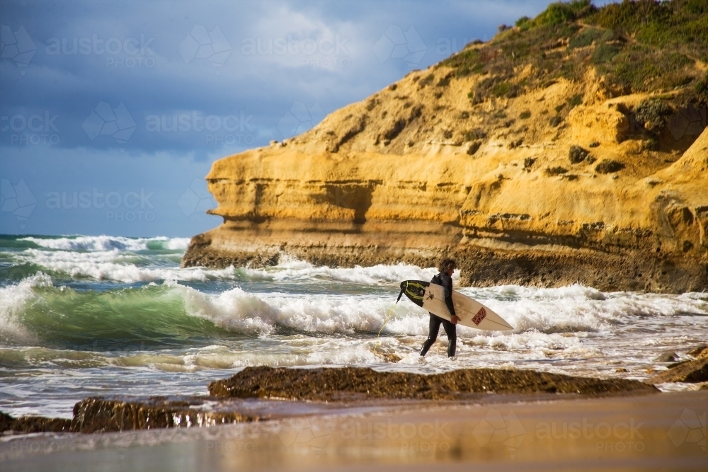 Surfer walking through shallows to a surf break - Australian Stock Image