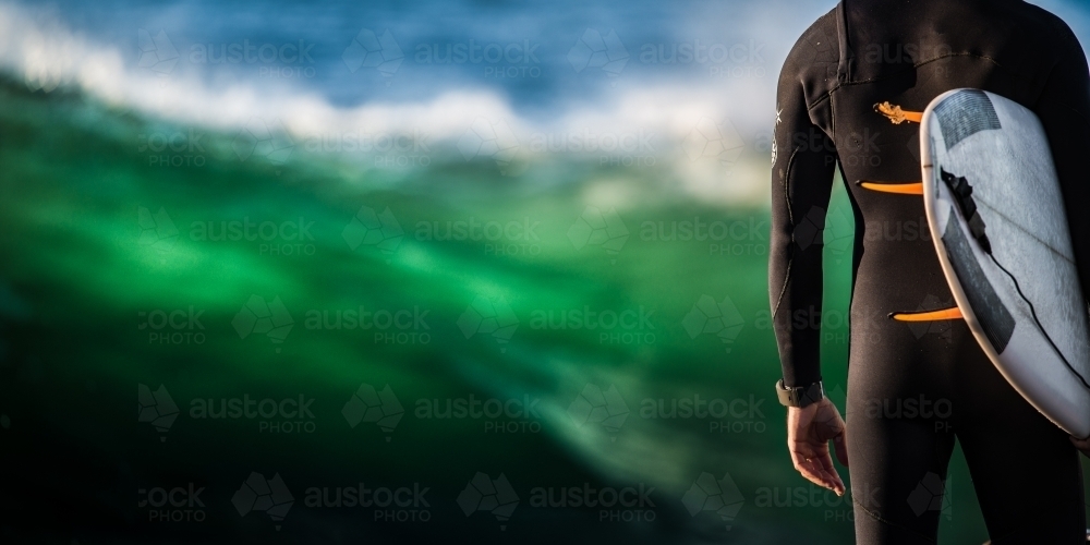 Surfer wearing full length wetsuit waiting to enter big surf - Australian Stock Image