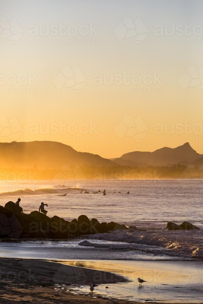 Surfers and people on rocks at sunset - Australian Stock Image