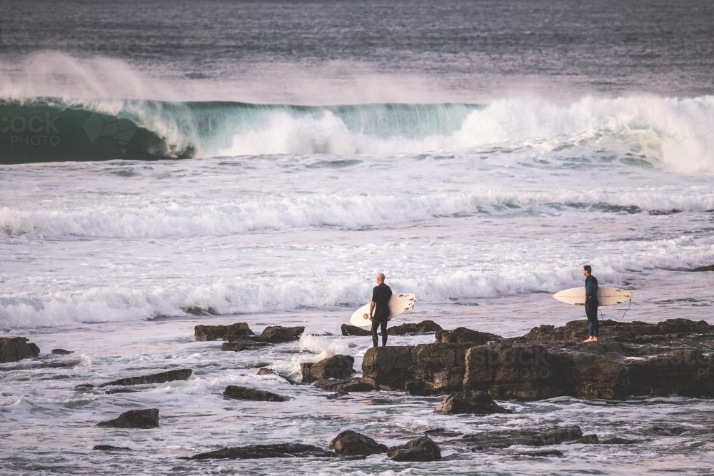 surfers getting ready to enter the ocean from rocks - Australian Stock Image