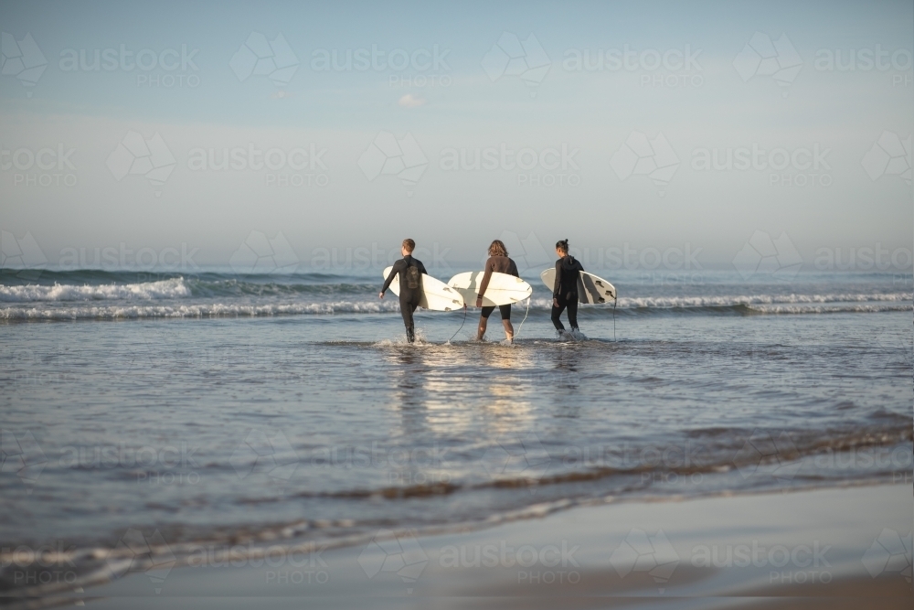 Surfers in distance running towards waves - Australian Stock Image