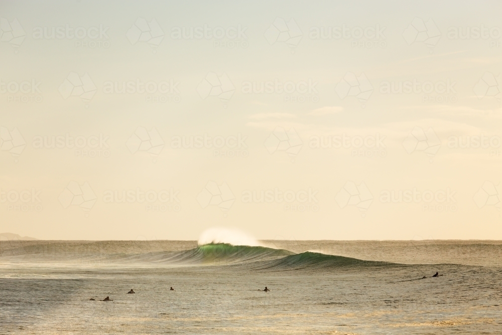 Surfers in the distance with breaking wave - Australian Stock Image