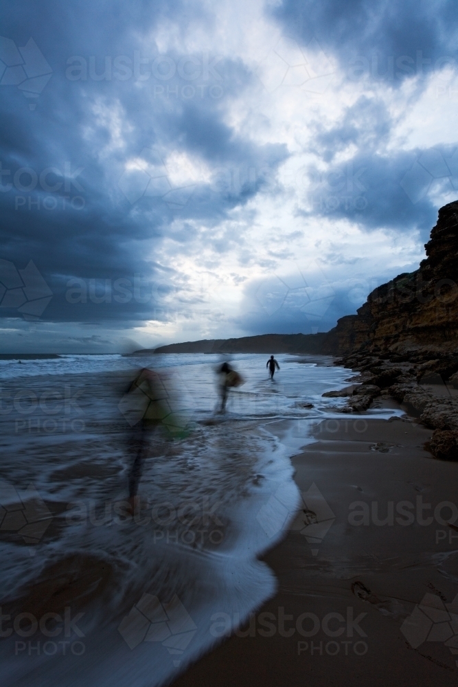 Surfers running through surf at dusk - Australian Stock Image