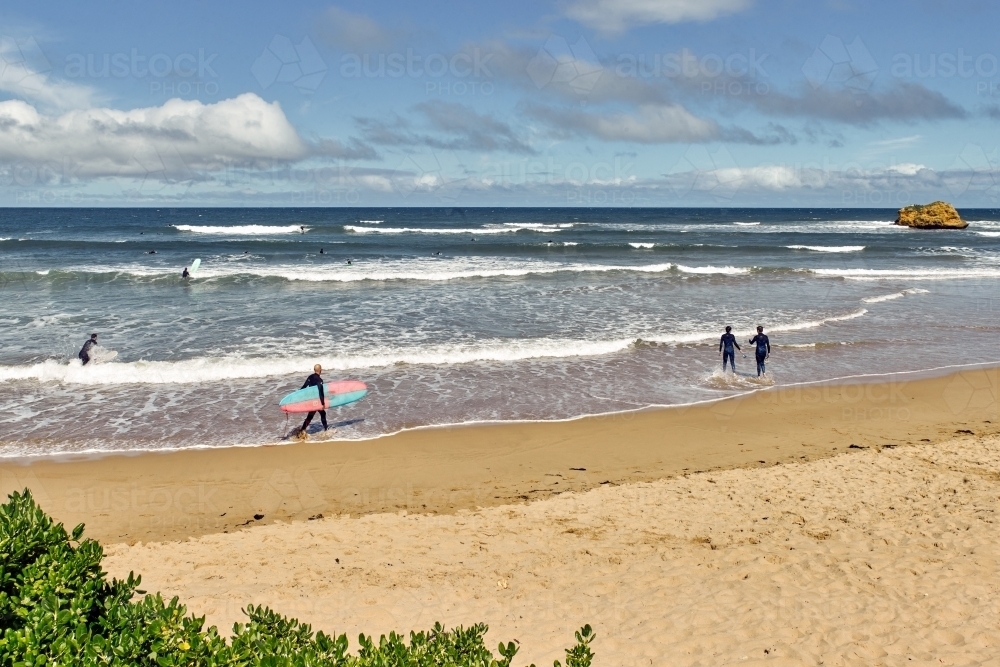 Surfers walking out and surfing at a surf beach - Australian Stock Image