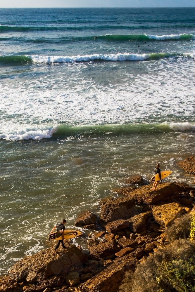 Surfers walking over rocks to a surf break - Australian Stock Image