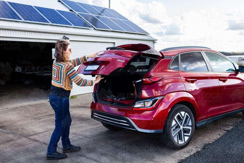 sustainable living concept - electric car and woman closing boot - Australian Stock Image
